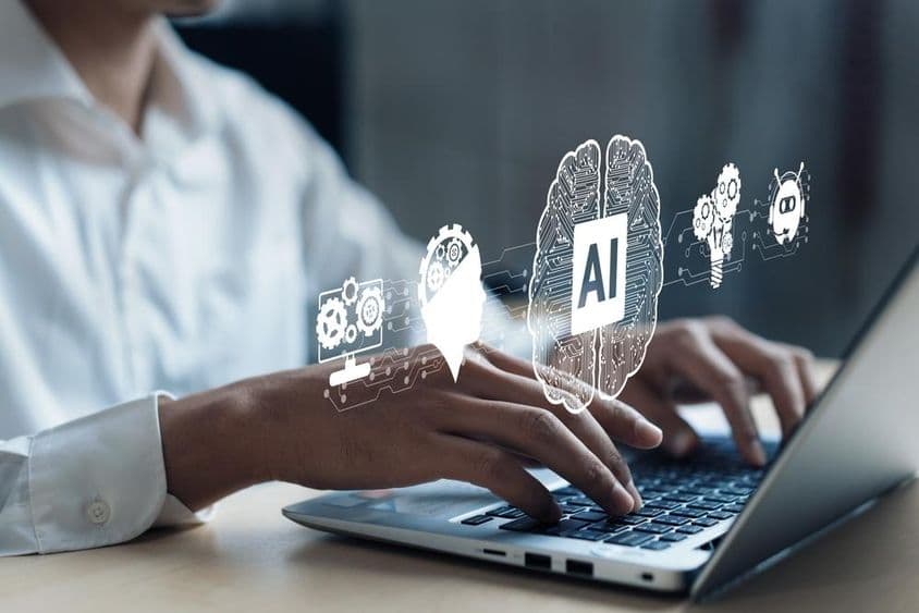 Проекция на ноутбуке, показывающая мозг ИИ и другие элементы. Человеческая рука работает на компьютере.