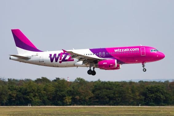 Самолет Wizz Air летит на низкой высоте с лесом на заднем плане.