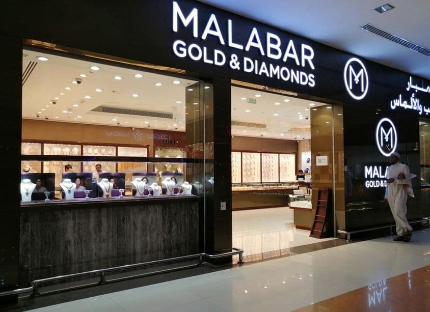 Эмиратец стоит перед витриной магазина Malabar Gold & Diamonds.