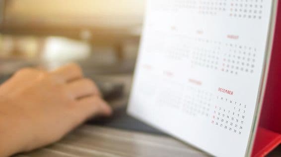 Рука рядом с календарем, месяцы размыты, декабрь четко виден.