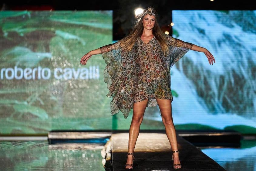 Выставка знака Roberto Cavalli на заднем плане, на переднем плане женская фигура в платье Roberto Cavalli на подиуме.