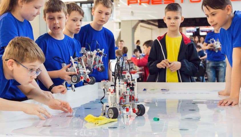Студенты в синих рубашках строят и программируют робота.