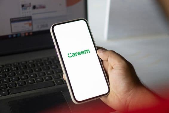 Рука держит телефон с работающим приложением Careem и блокнотом на заднем плане.