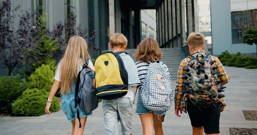 Ученики несут рюкзаки перед входом в школу.