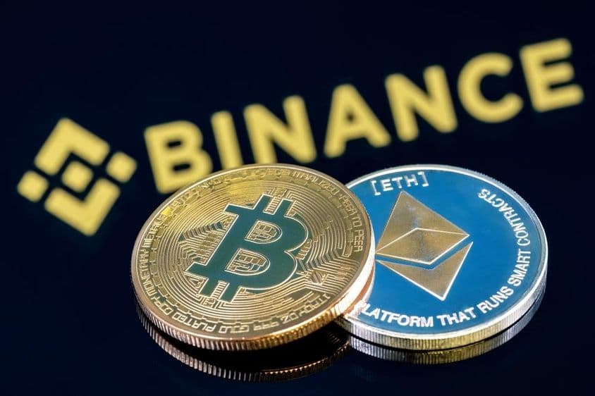 Надпись Binance на заднем фоне на черном столе с Биткоином и монетой Эфириум.