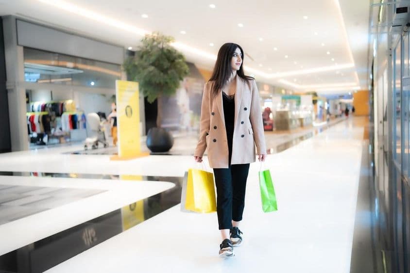 Женщина шопингует в Dubai Mall с двумя сумками на фоне магазинов.
