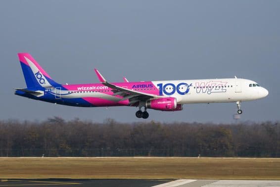 Самолет Wizz Air летит на низкой высоте над взлетно-посадочной полосой.