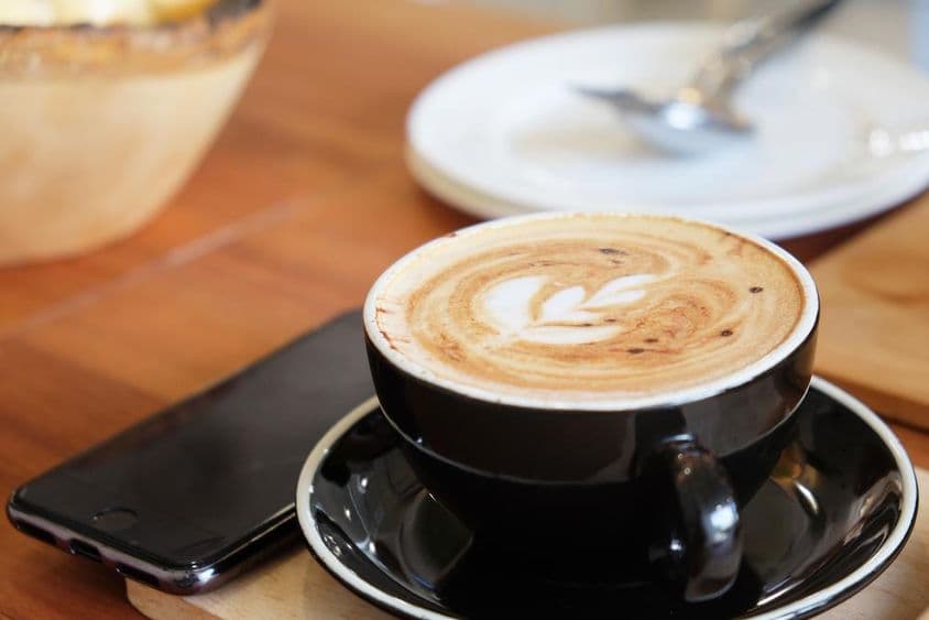 Чашка капучино на столе с телефоном рядом.