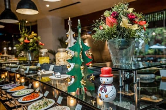Маленький снеговик в ресторане на прилавке с овощами рядом с деревянной рождественской ёлкой.