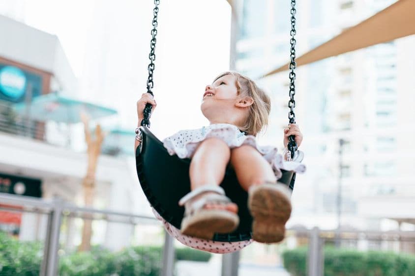 Счастливая маленькая девочка качается на качелях в детском саду.