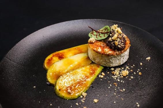 Жареный козий сыр с карамелизированной грушей, поданный в высоком стиле.