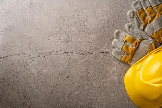 Перерыв на работе, желтая каска и рабочие перчатки на потрескавшейся бетонной поверхности.