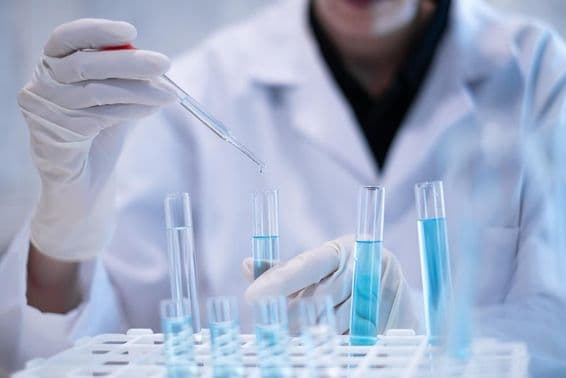 Учёный пипеткой вливает синюю жидкость в пробирку в лаборатории.