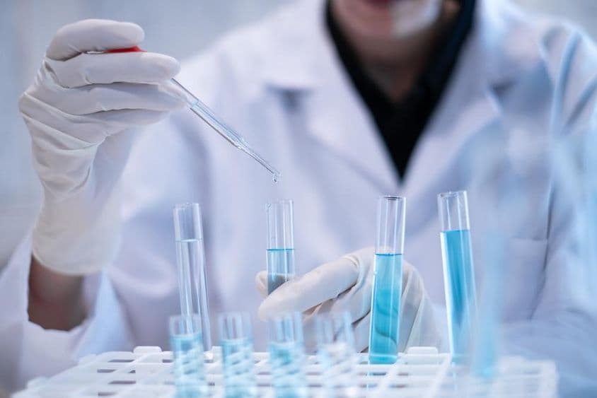 Учёный пипеткой вливает синюю жидкость в пробирку в лаборатории.