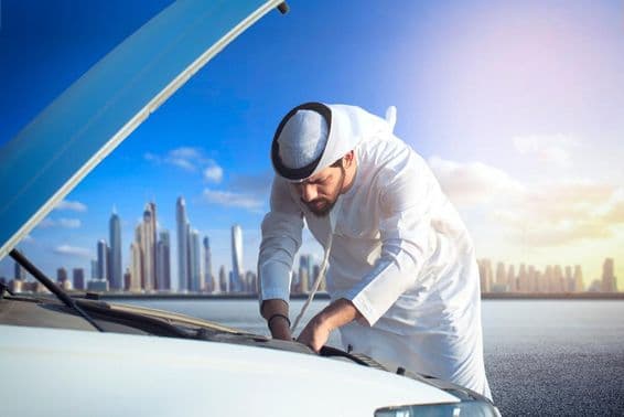 Арабский мужчина осматривает свой автомобиль, капот открыт.