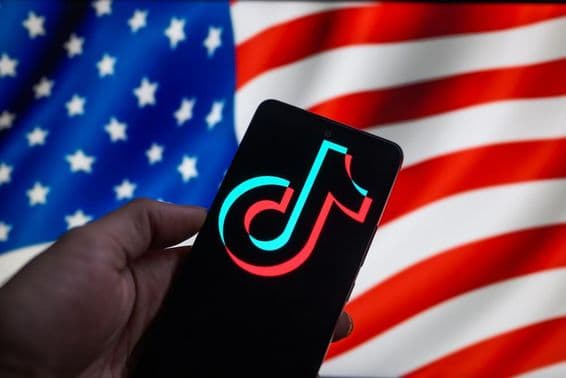 Логотип TikTok на смартфоне с флагом США на заднем плане.