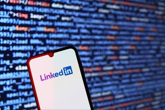 Смартфон с логотипом LinkedIn и фрагментом кода на заднем плане.