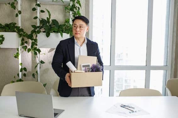 Мужчина увольняется с работы, складывая личные вещи в картонную коробку.