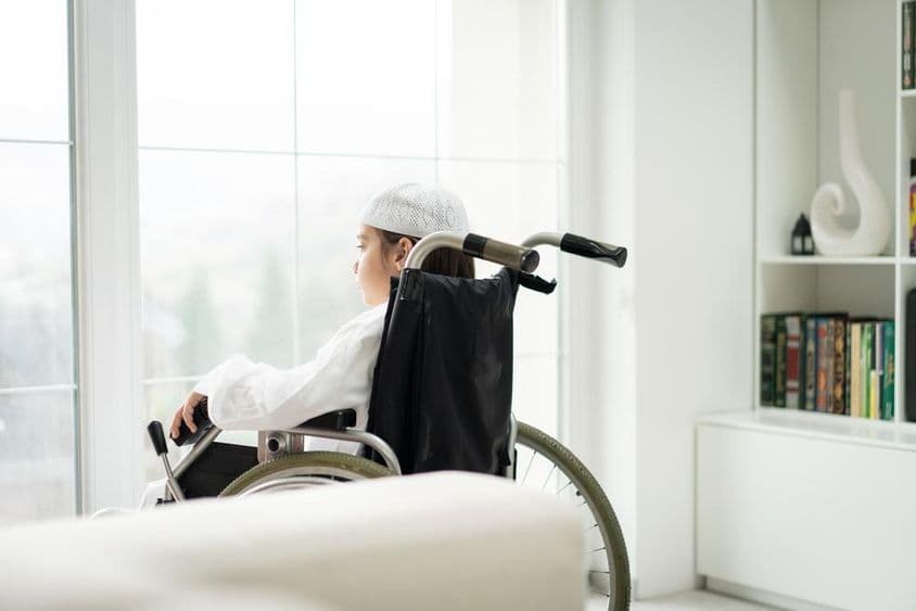 Мальчик в инвалидной коляске смотрит в окно.