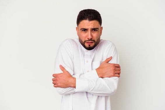 Молодой араб в традиционной одежде дрожит от холода.