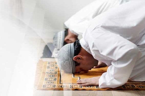 Исламские мужчины, одетые в белое, кланяются в молитве.