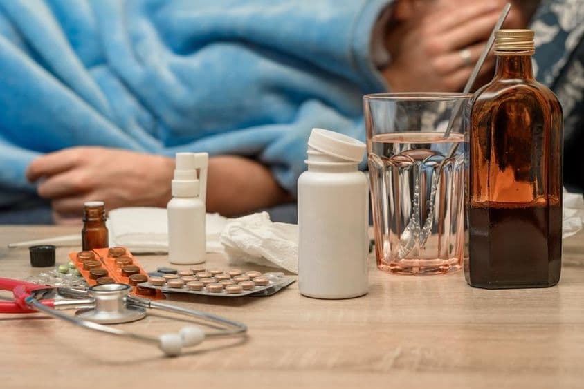 Мужчина с простудой и температурой лежит в постели.