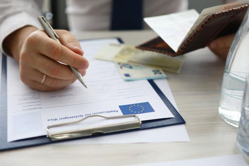 Человек с паспортом, вводящий личные данные в заявлении на получение шенгенской визы.