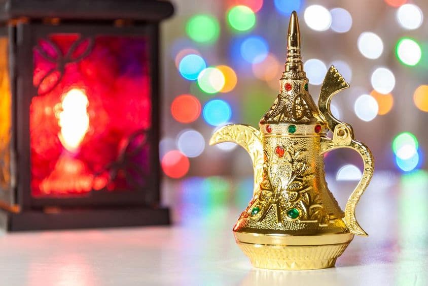 Арабская кофейная турка и лампа с яркими нечеткими огнями на фоне.