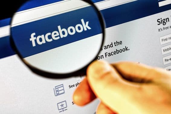 Скриншот главной страницы Facebook на мониторе через увеличительное стекло.
