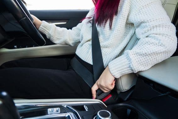 Женщина-водитель пристёгивает ремень безопасности.