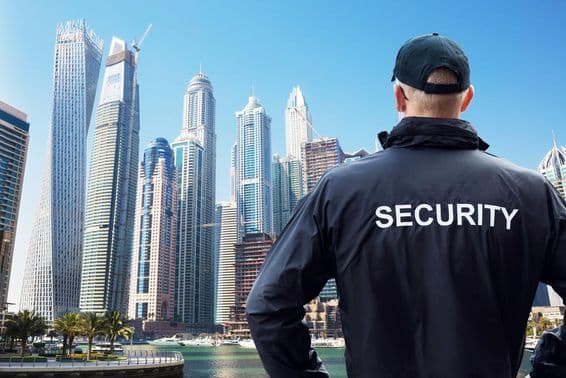 Мужчина-охранник, стоящий и смотрящий на город сзади.