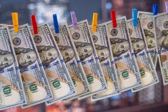 Купюра в 100 долларов США, висящая на бельевой веревке с деревянными прищепками.