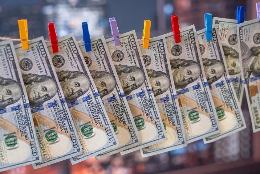 Купюра в 100 долларов США, висящая на бельевой веревке с деревянными прищепками.