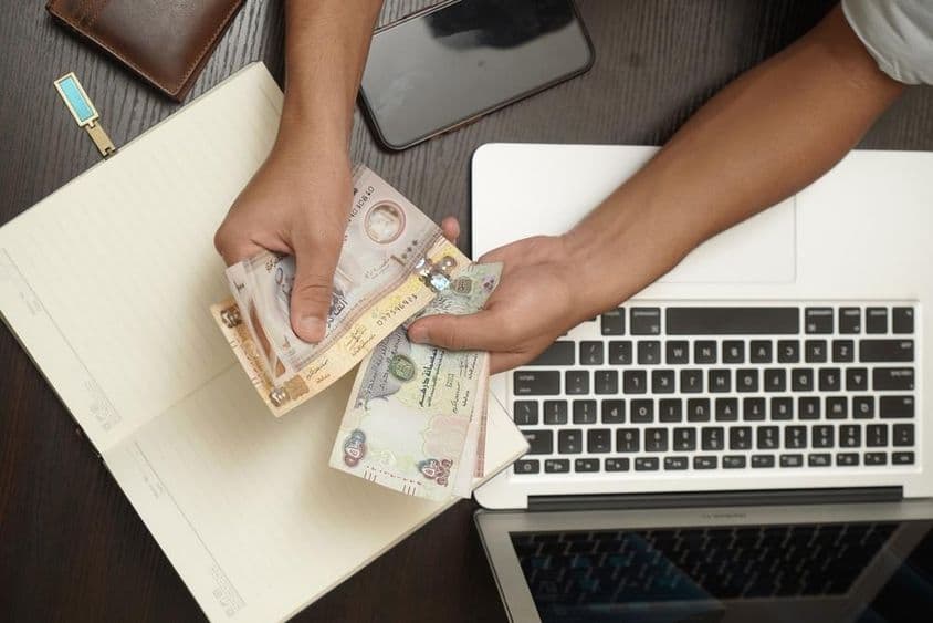 Мужчина считает пачку дирхамов Объединенных Арабских Эмиратов.