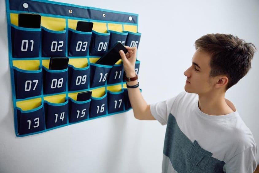 Ученик оставляет смартфон в настенном держателе для телефонов.