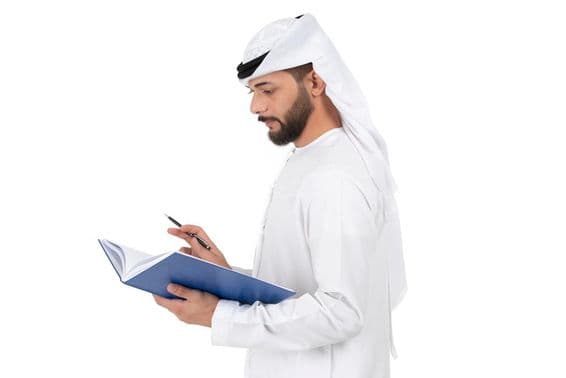 Молодой арабский учитель стоит и пишет в книге.