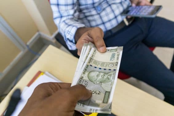 Человек передает 500-рупиевую индийскую банкноту другому человеку.