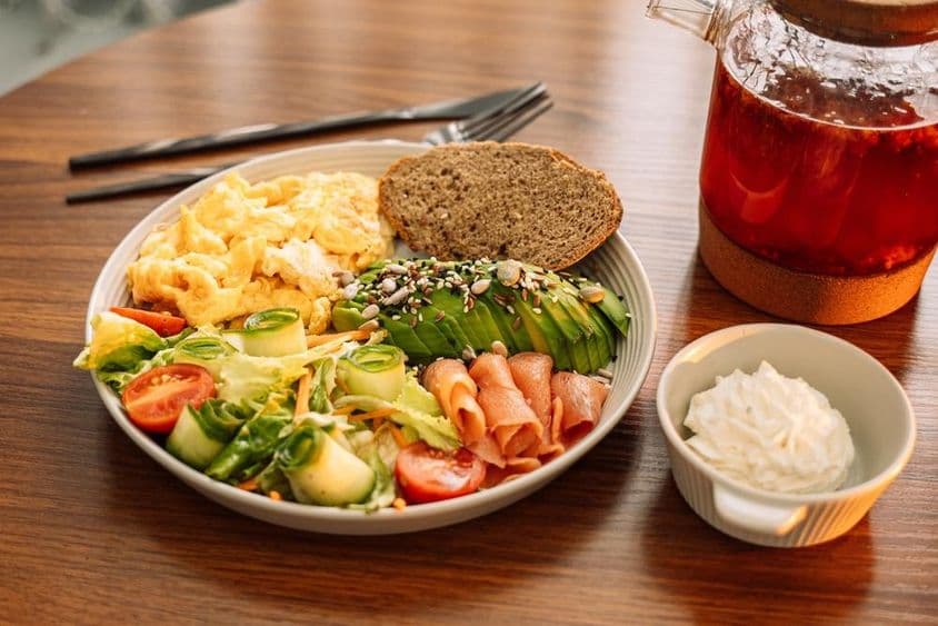 Здоровый завтрак с яйцами, авокадо, зеленью, салатом и малиновым чаем.