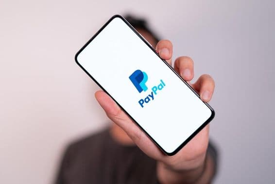 Мужчина с телефоном, на экране которого видно логотип PayPal.