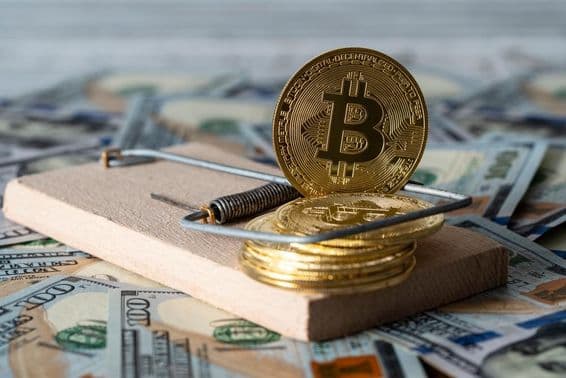 Золотые монеты криптовалюты биткойн в мышеловке, в фоне счета 100 долларов США.