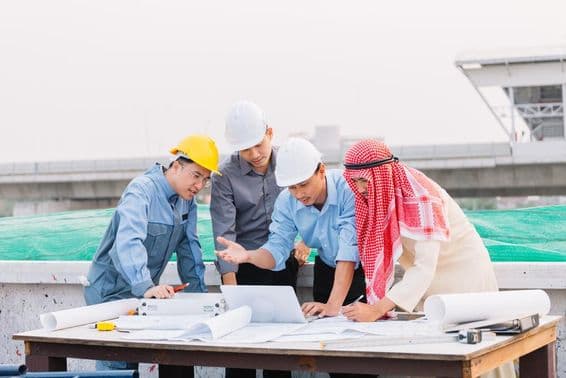 Арабский бизнесмен, инженер и рабочий обсуждают планы строительства, используя ноутбук.