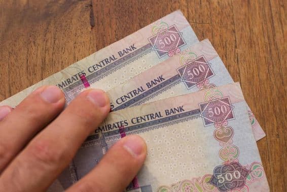 Люди держат валюту Объединенных Арабских Эмиратов (ОАЭ)